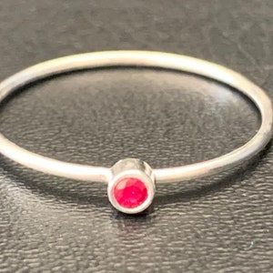 May include: A simple silver band ring with a small, bright red gemstone set in the centre.