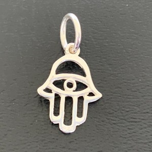 May include: A silver charm in the shape of a Hamsa hand with an eye in the center. The charm is designed to bring good luck and protection.