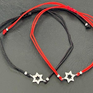 May include: Two friendship bracelets with black and red string, each with a silver star charm.