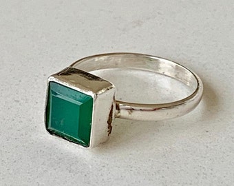 Puede incluir: Un anillo de plata con una piedra preciosa verde cuadrada engastada en un engaste de plata.