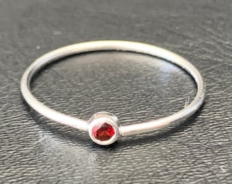 May include: A simple silver band ring with a small, round, red gemstone.