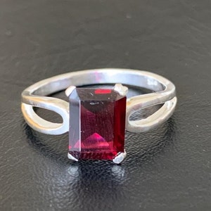 May include: A silver ring with a dark red, emerald-cut gemstone.