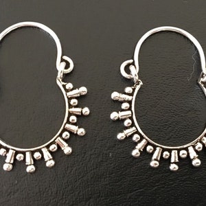 Peut inclure: Une paire de boucles d'oreilles créoles en argent avec un motif décoratif de petites perles et de pointes autour du cercle.
