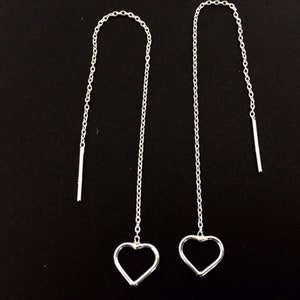 May include: A pair of silver heart shaped dangle earrings with a thin chain and a small silver bar at the end of each chain.