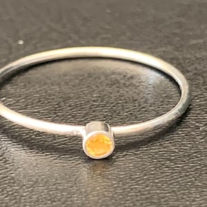 May include: A simple silver ring with a small, round, orange gemstone.