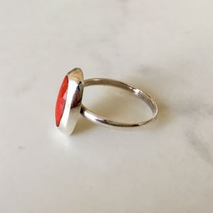 Pu&ograve; includere: Un anello d'argento con una pietra ovale rossa. L'anello &egrave; incastonato su una fascia semplice e ha una finitura lucida.