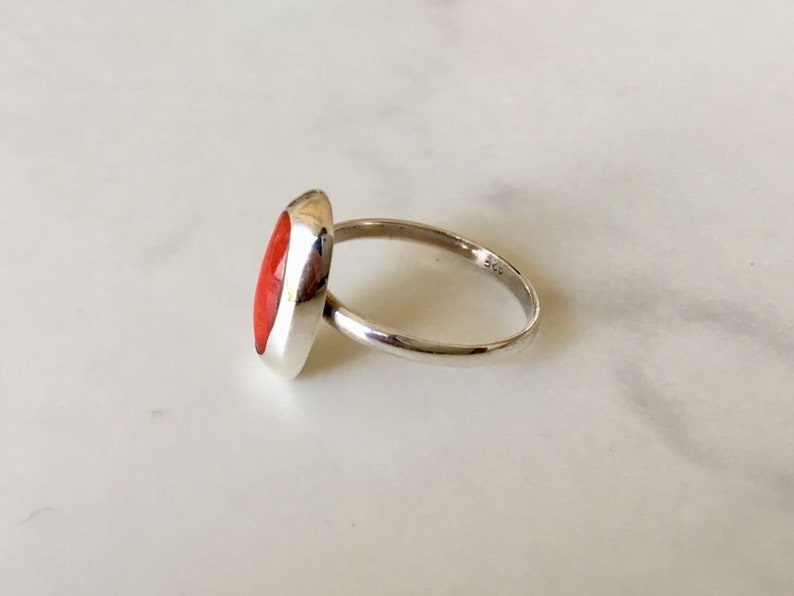 Pu&ograve; includere: Un anello d'argento con una pietra ovale rossa. L'anello &egrave; incastonato su una fascia semplice e ha una finitura lucida.