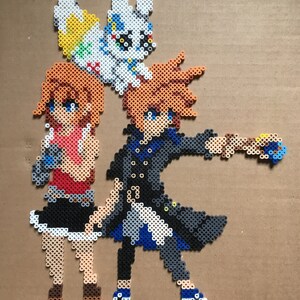 May include: A pixel art bead sprite of three characters. A girl with orange hair and a red shirt stands next to a boy with orange hair and a blue shirt. A white and yellow creature with rabbit ears stands on top of the girl's head.