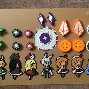 May include: A collection of colorful pixel art characters and objects made with perler beads. The characters are all female and are wearing different outfits. The objects include a purple and white eye, a blue and white circle, and a green and white star.
