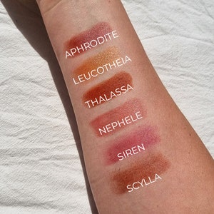 A skin swatch of all the tinted lip balms on the underside of the forearm on fair skin, to show how they appear when applied. Top of image to bottom: Aphrodite, Leucotheia, Thalassa, Nephele, Siren and Scylla