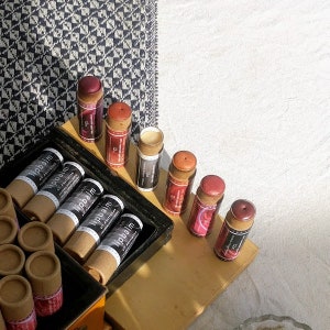 Puede incluir: Una colecci&oacute;n de tubos de b&aacute;lsamo labial en varios colores, incluyendo rojo, rosa y naranja. Los tubos est&aacute;n hechos de cart&oacute;n y tienen una etiqueta negra con el texto "Lipbalm All Australian" impreso en ellos.