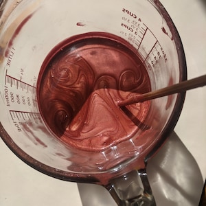 Tinted lip balms in the making (in the shade Nephele, a lovely peachy pink). A top view of the mixture before pouring showing the beautiful swirls from the shimmery pigments in the molten balm
