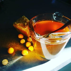 The untinted lip balm in the making - a glass jug of the molten mixture next to a block of beeswax and some macadamia nuts in order to highlight the two ingredients that comprise this balm - raw Victorian beeswax and macadamia oil