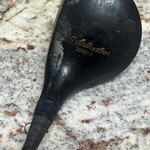 Pu&ograve; includere: Un'antica mazza da golf con una testa in legno scuro e usurato e un lungo manico sottile. La testa della mazza presenta segni di usura visibili, con il testo "A.G. Spalding Bros. DUNDEE" inciso sulla superficie. L'impugnatura &egrave; avvolta con un'impugnatura scura.