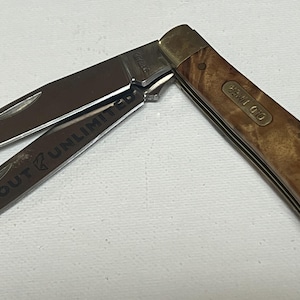 May include: A pocket knife with two open blades. The blades are silver and the handle is wood-toned with brass accents. One blade has the text "TROUT UNLIMITED". The handle has the text "OLD TIMER".