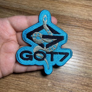 May include: A blue and black embroidered patch with a snake design and the text "GOT7".
