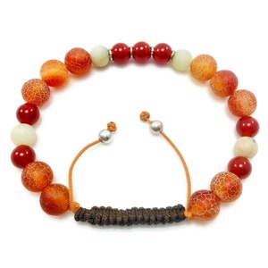 May include: A red, orange, and white beaded bracelet with a brown cord closure. The bracelet is made of natural stones and has a simple, elegant design.