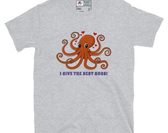 Puede incluir: Camiseta gris claro con un pulpo de dibujos animados con tentáculos naranjas y corazones rojos. El pulpo tiene ojos grandes y está centrado en la camiseta. El texto "I GIVE THE BEST HUGS!" está debajo del pulpo.