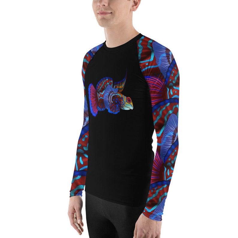 May include: A black long-sleeve rash guard with a colorful fish design on the front and abstract patterns on the sleeves. The fish is red, blue, and green with a white outline.