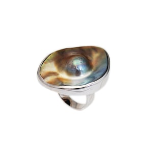 Könnte beinhalten: Ein silberner Ring mit einem großen, schillernden Abalone-Muscheleinsatz in der Mitte. Die Muschel hat eine einzigartige, organische Form und eine Vielzahl von Farben, darunter Braun, Grün und Blau.
