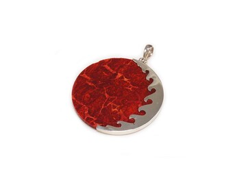 Puede incluir: Un colgante redondo de coral rojo con un diseño de olas plateadas alrededor del borde. El colgante tiene una anilla plateada para sujetarlo a una cadena.