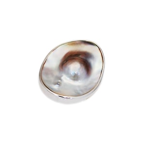 Könnte beinhalten: Eine weiße Perlmuttschale mit silbernem Rand. Die Schale ist oval geformt und leicht gewölbt.