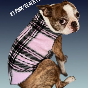 May include: A Boston Terrier wearing a pink and black plaid fleece dog sweater. The sweater has a turtleneck collar and is labeled #1 PINK/BLACK PLAID.