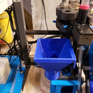 May include: A blue plastic funnel attached to a metal frame. The funnel is used to feed small objects into a machine.