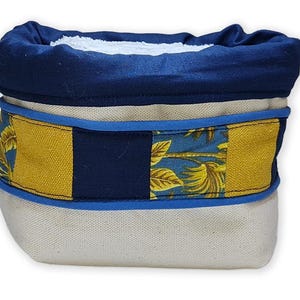 Peut inclure: Un panier de rangement en tissu avec un dessus roulé bleu marine et une bande de tissu à motifs jaune et bleu. Le panier a un intérieur blanc et une bordure bleu clair. Le motif du tissu comprend des feuilles de palmier.