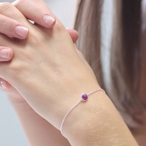May include: A delicate silver chain bracelet with a single, small, round, purple gemstone.