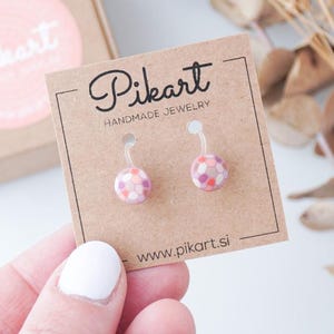 Può includere: Un paio di orecchini Pikart fatti a mano con un design colorato e fantasia. Gli orecchini sono esposti su un cartoncino marrone con il logo e il sito web di Pikart. Una piccola scatola regalo marrone con un logo rosa è sullo sfondo.