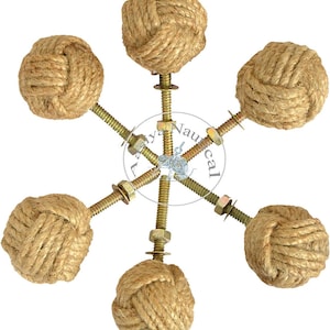 Può includere: Un elemento decorativo a tema nautico con sei nodi di corda fissati a una struttura metallica centrale con bulloni e dadi. I nodi sono realizzati in corda color naturale e l'hardware metallico ha una finitura dorata.