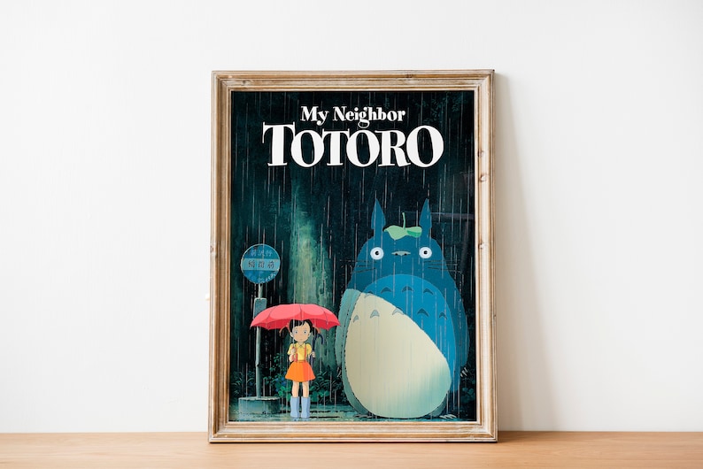 May include: A framed poster featuring a blue and white cartoon character, Totoro, standing in the rain with a young girl holding a red umbrella. The poster has the text "My Neighbor Totoro" in white letters.