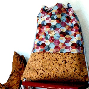 May include: A colorful drawstring bag with a geometric pattern and a cork bottom. The bag is made of fabric and has a drawstring closure.