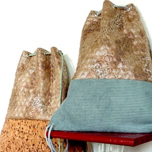 Può includere: Due sacche a cordoncino realizzate con materiali diversi. La sacca a sinistra è marrone con un fondo in sughero. La sacca a destra è marrone con un fondo blu chiaro.