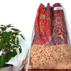 Op de afbeelding: Een rode en bruine trekkoordtas met een kurken bodem. De tas heeft een bedrukt ontwerp van een traditioneel tapijt. De tas heeft een wit trekkoord en een label met de tekst "talida".