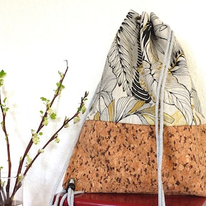 May include: A drawstring bag made of cork and fabric with a floral pattern. The bag has a light gray drawstring and a brown cork bottom.