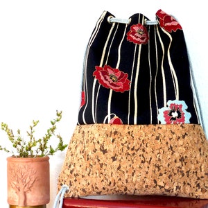 May include: A black and white striped drawstring bag with red poppy flowers and a cork bottom.