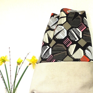 May include: A drawstring bag with a black, white, gray, pink, and orange geometric pattern. The bag has a beige corduroy bottom.