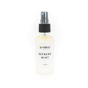 Puede incluir: Una botella de vidrio transparente con un pulverizador negro. La botella est&aacute; etiquetada con "sunflower motherhood" y "REFRESH MIST".