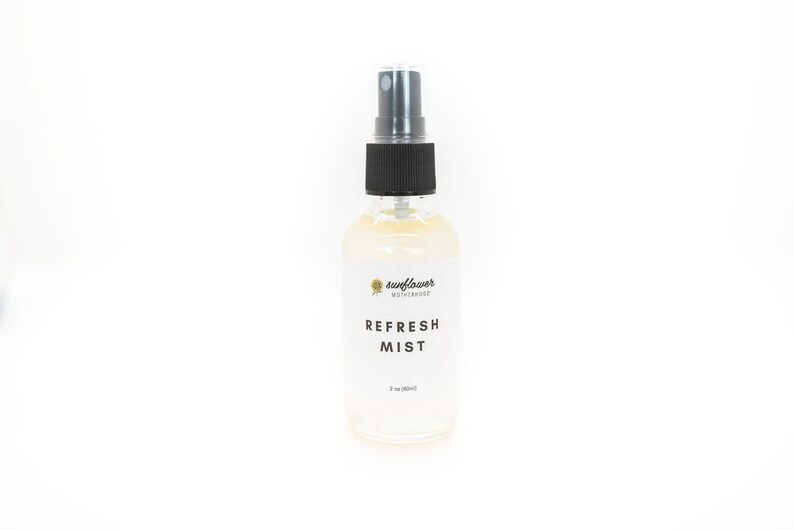 Puede incluir: Una botella de vidrio transparente con un pulverizador negro. La botella est&aacute; etiquetada con "sunflower motherhood" y "REFRESH MIST".