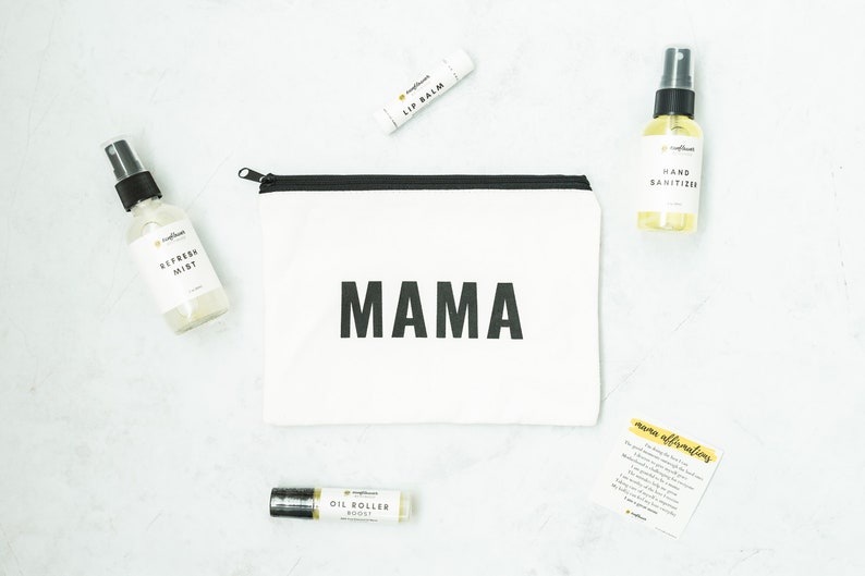 Puede incluir: Una bolsa de lona blanca con cremallera con la palabra "MAMA" impresa en negro. La bolsa est&aacute; rodeada de varios frascos y tubos peque&ntilde;os, incluyendo un b&aacute;lsamo labial, un desinfectante de manos y un rodillo de aceite esencial. Tambi&eacute;n se puede ver una tarjeta con el texto "afirmaciones de mam&aacute;".