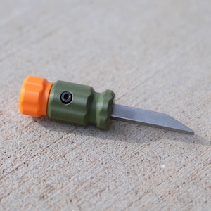 May include: A small, olive green and orange utility knife with a silver blade. The knife has an orange, ridged cap and a silver blade extending from the olive green handle. The knife is designed for precision cutting tasks.