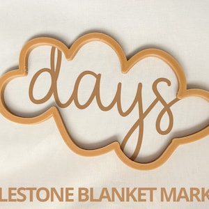 Pode incluir: Um marcador de manta de marco em forma de nuvem marrom com a palavra "dias" escrita em itálico.