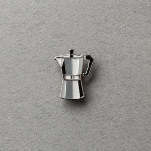 Peut inclure: Épingle à café en argent et émail avec des rayures verticales noires, blanches et grises. L'épingle est une réplique miniature d'une cafetière à expresso, avec une poignée et un couvercle. L'épingle est posée sur un fond gris.