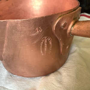 May include: A copper saucepan with a handle and a stamped mark that reads "CH. TROTTIER, Succr. A. DELAVERNE, 23 RUE MONTMARTE, PARIS". The number "15" is stamped on the side of the pan.