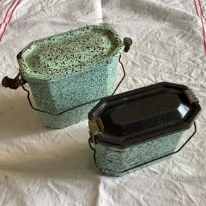 以下が含まれることがあります： 斑点のある緑と黒の塗装が施された、ビンテージの金属製ランチボックス2個。ボックスにはヒンジ付きの蓋と持ち運び用のハンドルが付いています。