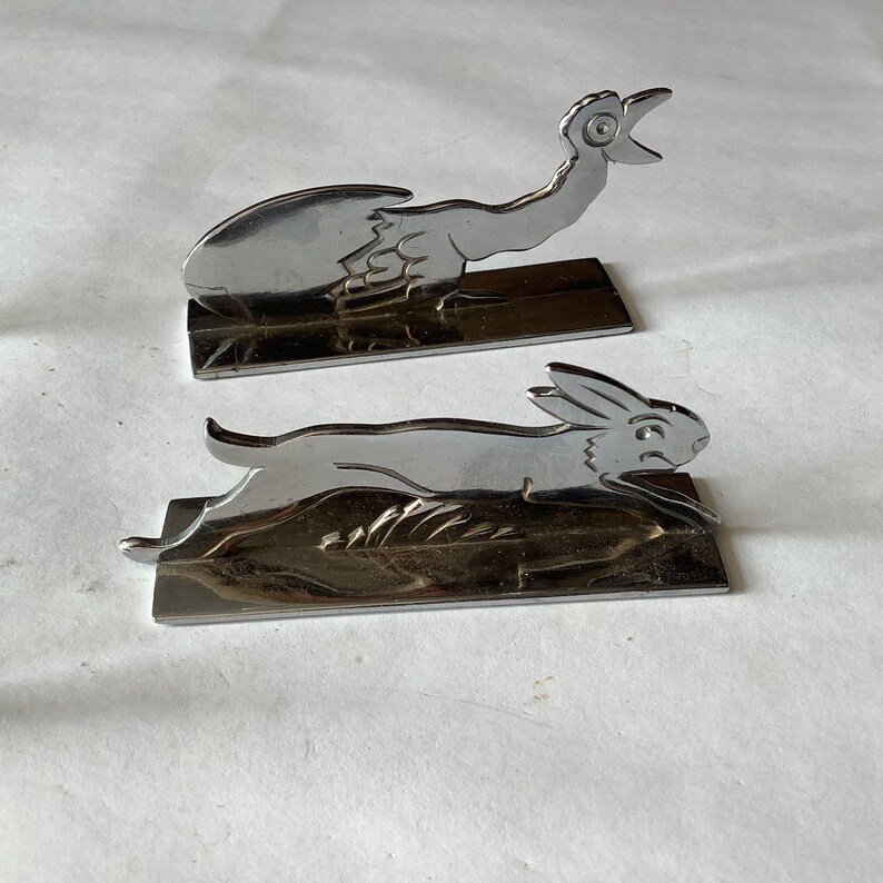 Pode incluir: Duas esculturas de metal cromado. Uma retrata um p&aacute;ssaro com o bico aberto, a outra um coelho correndo. Ambas s&atilde;o montadas em bases retangulares. As esculturas t&ecirc;m uma apar&ecirc;ncia met&aacute;lica reflexiva.