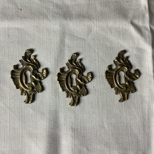 Può includere: Tre copri-chiavi in ​​ottone decorati con intricati motivi floreali.