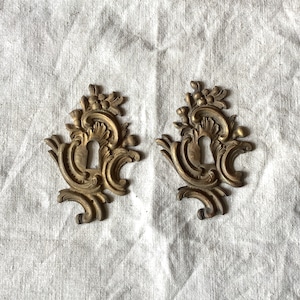 Può includere: Due copri-chiavi dorati decorati con intricati motivi floreali. I copri-chiavi sono in metallo e hanno un aspetto vintage.